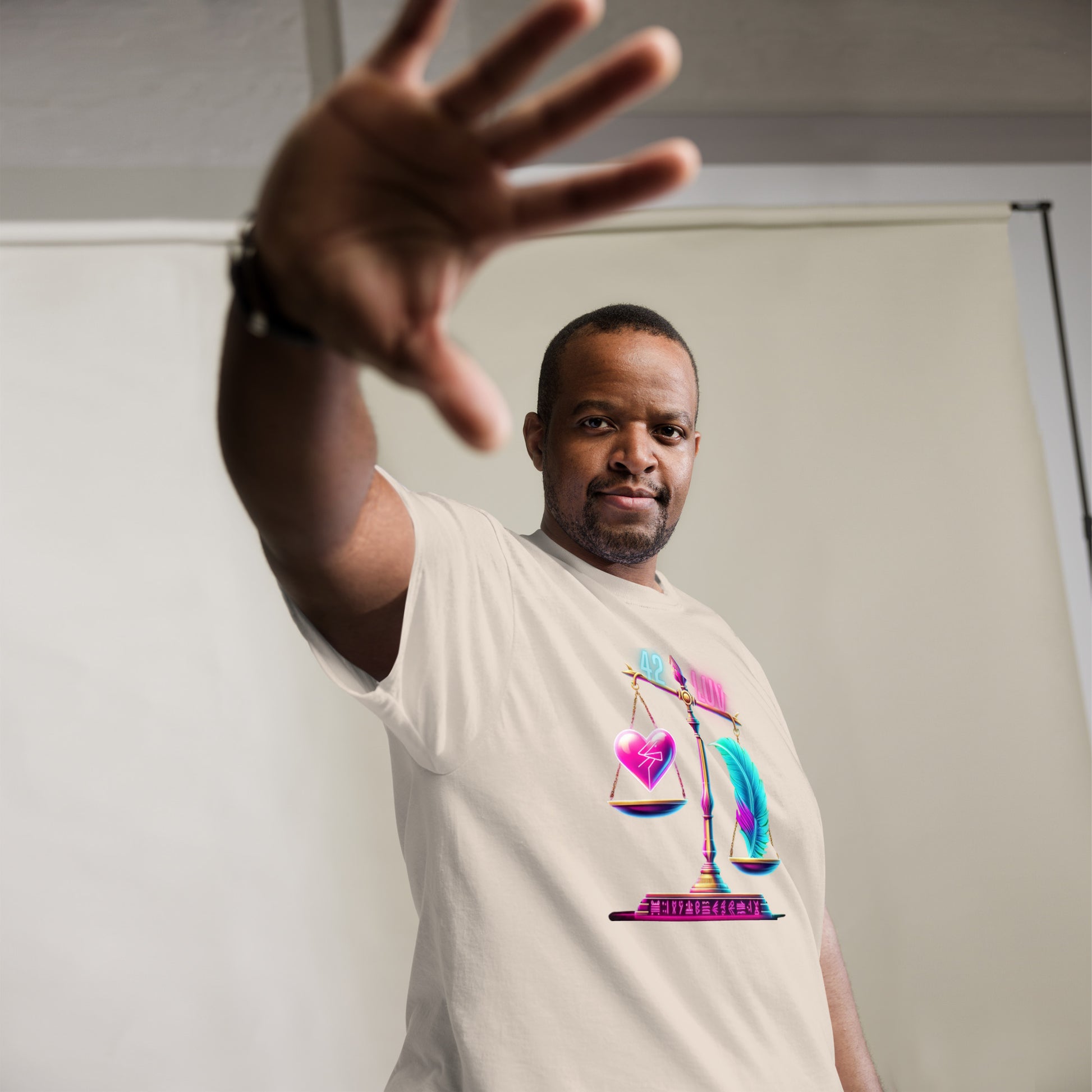 Fashionable Black Man Wearing a Cream T-Shirt with a Vibrant Design of a Heart and Feather on a Scale – Highlighting Unique Urban Fashion for Men with Symbolic Art Representing Balance and Equality, Captured in a Studio Setting