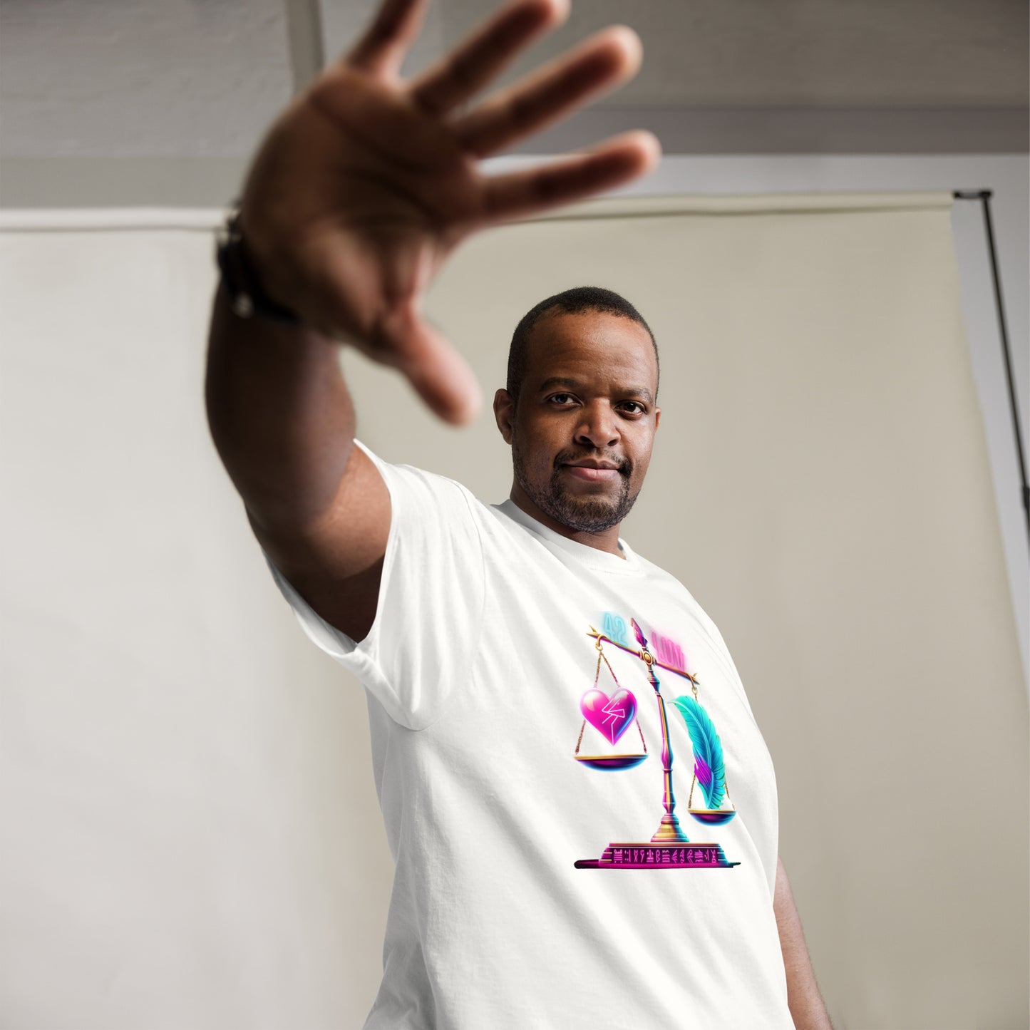 Stylish Black Man Wearing a White T-Shirt with a Colorful Scale Design Featuring a Heart and a Feather – Showcasing Unique Urban Fashion for Men with Symbolic Art Representing Balance and Equality, Captured in a Studio Setting